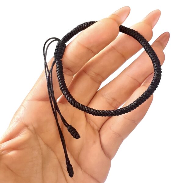 Pulsera Tibetanacolor negro de Cuerda sostenida en una mano con fondo blanco